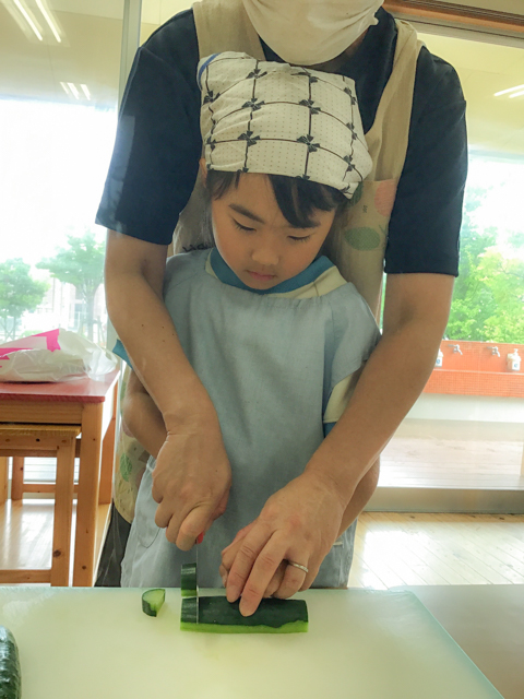 保育者と一緒に野菜を切る子ども
